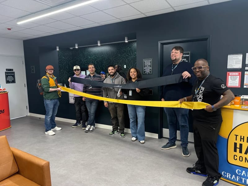 A line of people inside Curaleaf's Meriden store hold a yellow ribbon and a black ribbon across the lobby before the ribbon cutting.
