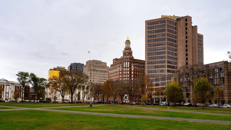 The New Haven Green's lawn and paths in fall, with downtown buildings along Church Street behind